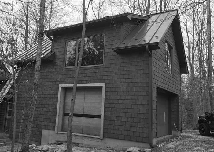 Petit garage en bardeau de cèdres dans le bois avec toit en métal et gouttières en aluminium
